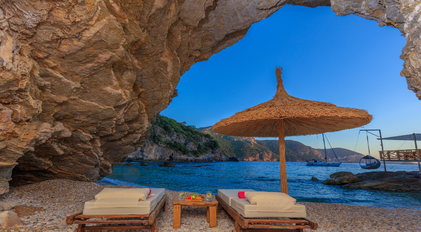 Shaded loungers set beside a natural cave opening on a quiet bay