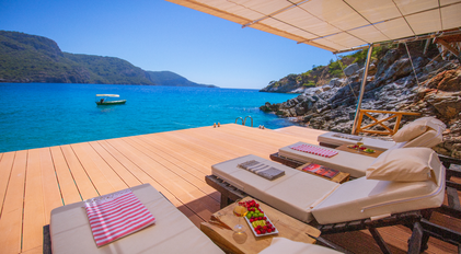 Loungers on a waterfront deck overlooking a wide turquoise Mediterranean bay