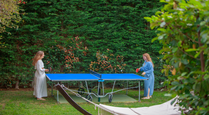 Guests playing relaxed garden table tennis beside dense Mediterranean greenery