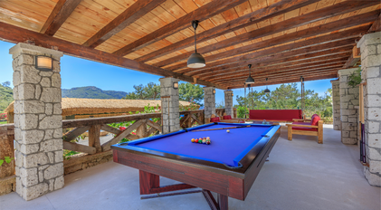 Outdoor pool table on a shaded Mediterranean terrace surrounded by forested hills