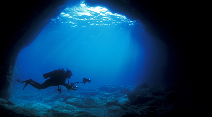 Scuba diver exploring an underwater cave illuminated by ethereal sun rays