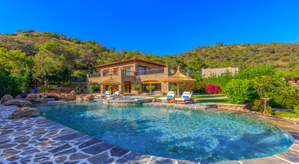 Stone villa with expansive pool terrace set against lush forested hills