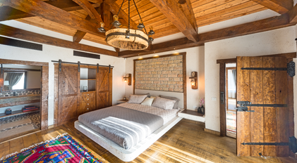 Rustic master bedroom with wooden beams, stone wall headboard and warm natural light