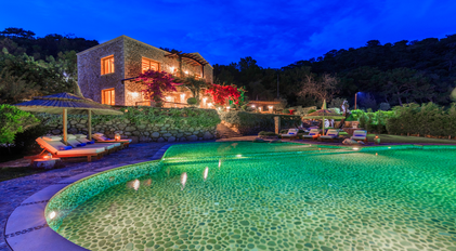 Night-lit stone villa overlooking a glowing organic-shaped pool