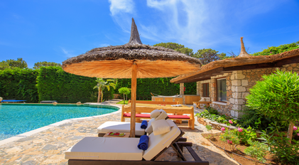 Shaded poolside loungers beside stone guesthouse terrace and Mediterranean greenery