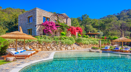 Stone villa with vibrant bougainvillea overlooking a natural-style Mediterranean pool