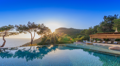 Infinity pool at sunrise overlooking Mediterranean sea and pine-covered cliffs