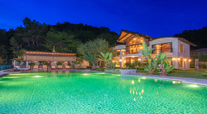 Night view of illuminated stone villa reflected over a glowing Mediterranean-style pool