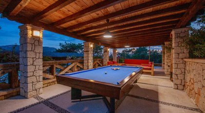 Outdoor billiards pavilion with stone columns overlooking a quiet Mediterranean setting