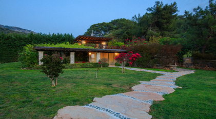 Stone villa facade surrounded by lush gardens and an evening-lit terrace