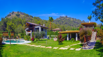 Wide panoramic view of stone villa, gardens and pool set against forested mountains