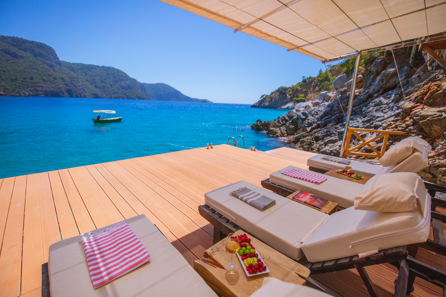 Loungers on a waterfront deck overlooking a wide turquoise Mediterranean bay