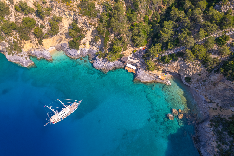 Aerial view of a secluded private bay with yacht anchorage along a forested Mediterranean coastline