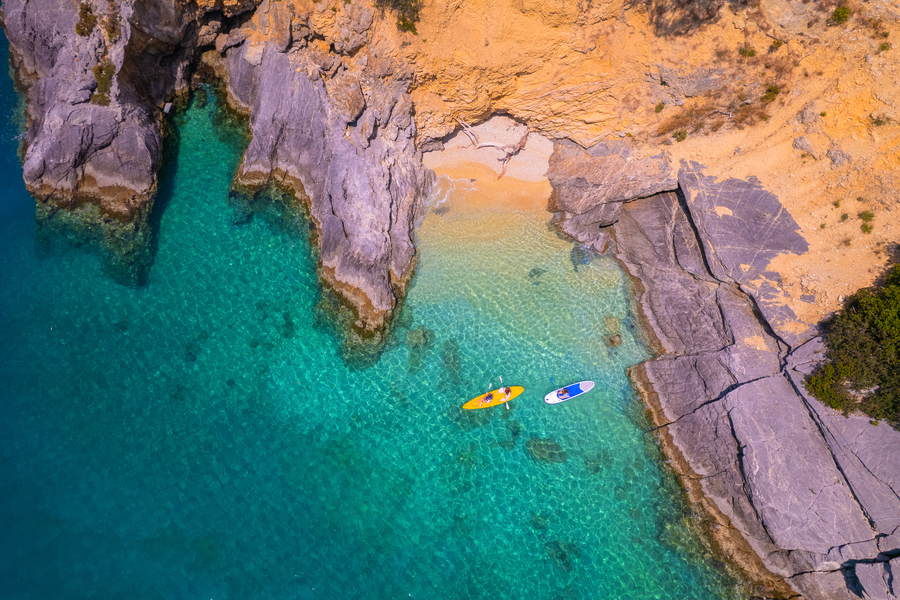 Aerial view of a hidden cove with SUP and kayak over crystal-clear turquoise waters