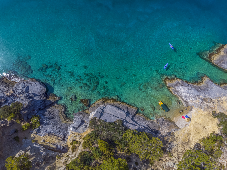 Aerial view of shallow turquoise coastline with rock formations and kayaks
