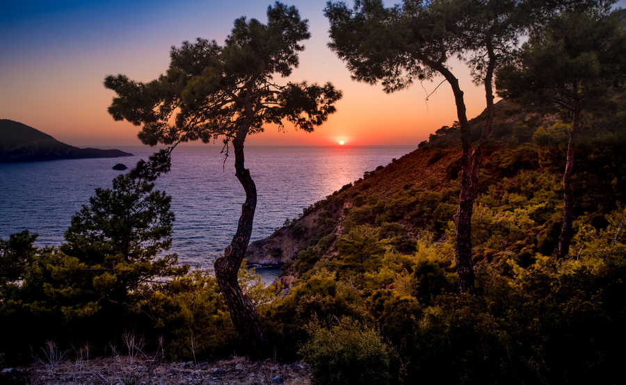 Sunset over a forested Mediterranean ridge overlooking a secluded coastal bay