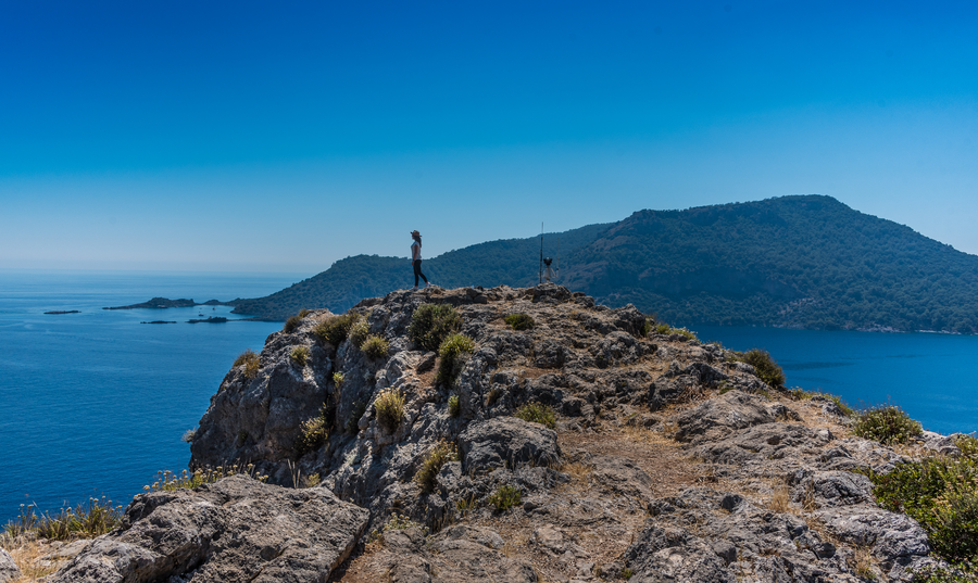 Hiker standing on a rugged clifftop overlooking the Mediterranean peninsula coastline
