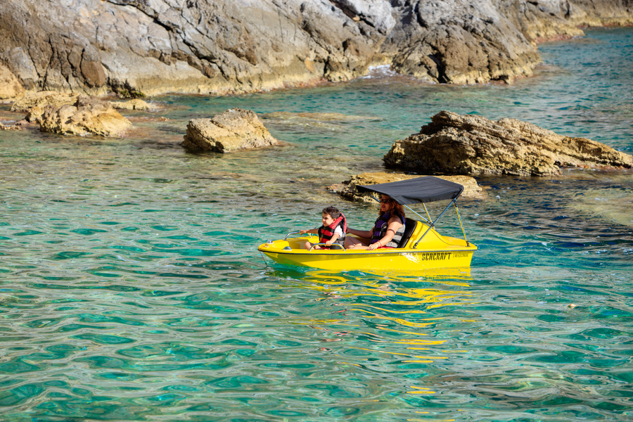 Pedal boat drifting through a calm turquoise cove beneath rugged Mediterranean cliffs