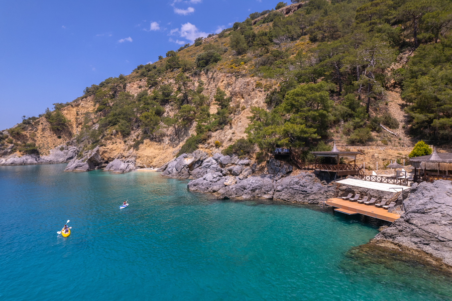 Kayaks and paddleboards exploring a calm turquoise Mediterranean bay near a secluded wooden jetty
