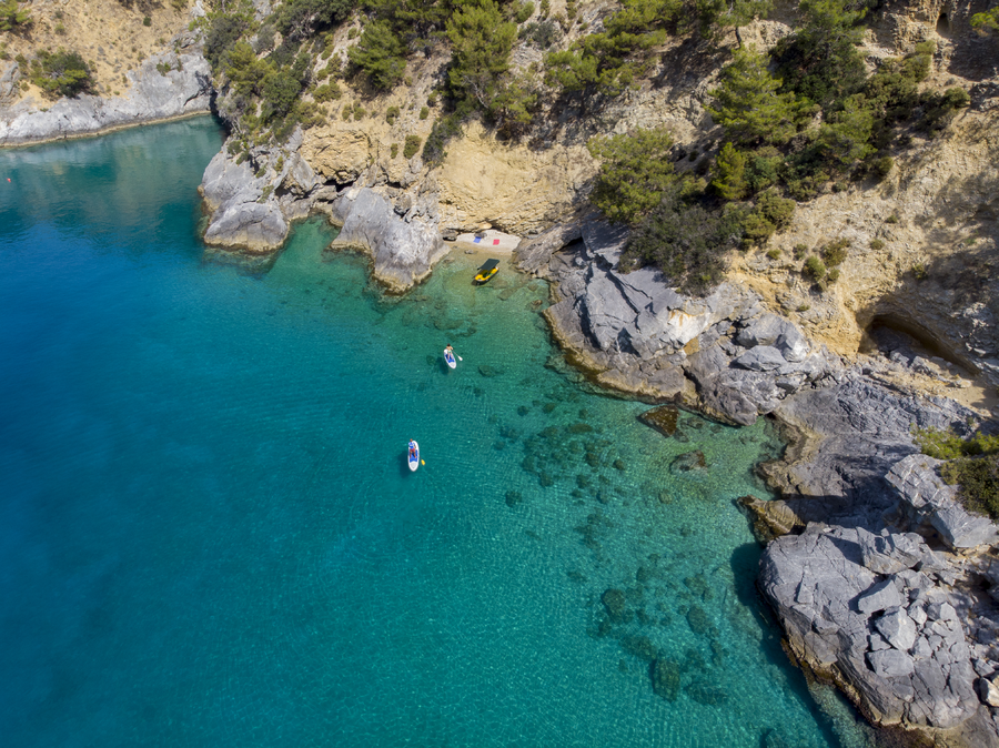 Aerial view of paddleboarders gliding across a clear turquoise Mediterranean cove