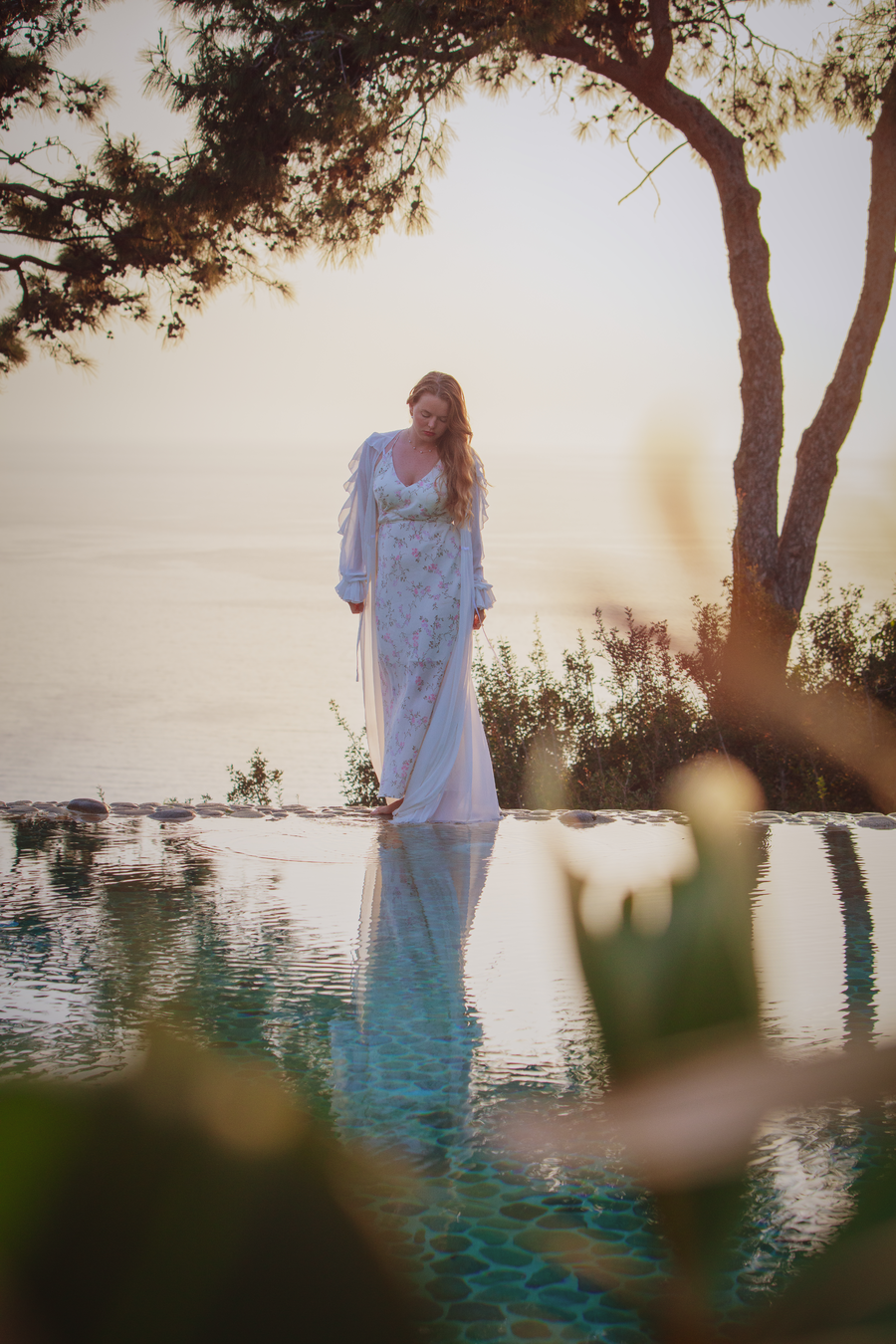 Bride standing by an infinity pool at sunrise overlooking a quiet bay
