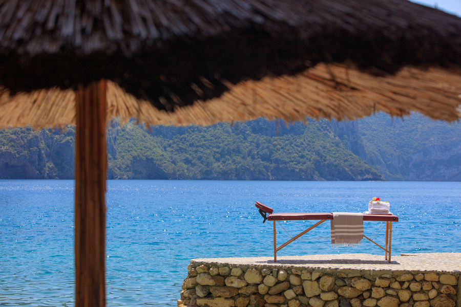 Seaside massage table overlooking a calm private bay beneath rugged cliffs