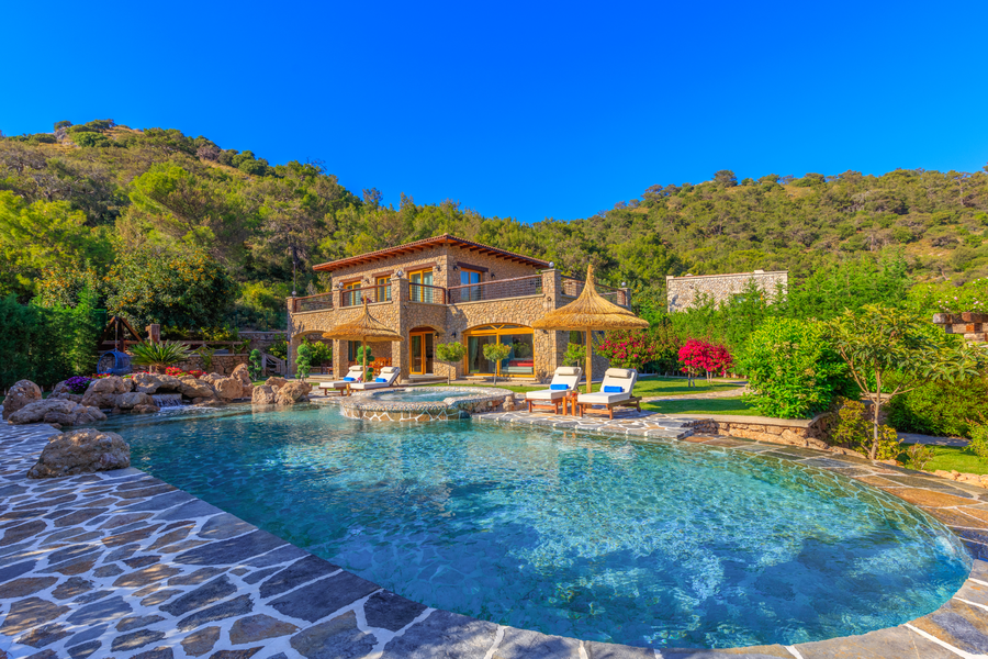 Stone villa with expansive pool terrace set against lush forested hills