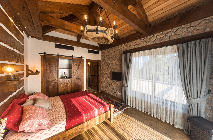 Rustic master bedroom with wooden beams, stone walls and large window view