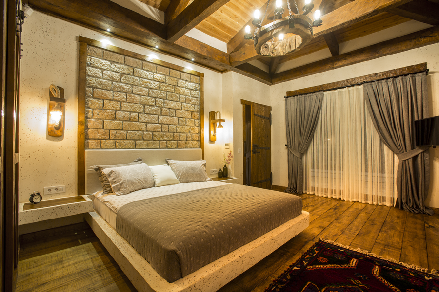 Warm master bedroom with stone accent wall and rustic wooden ceiling