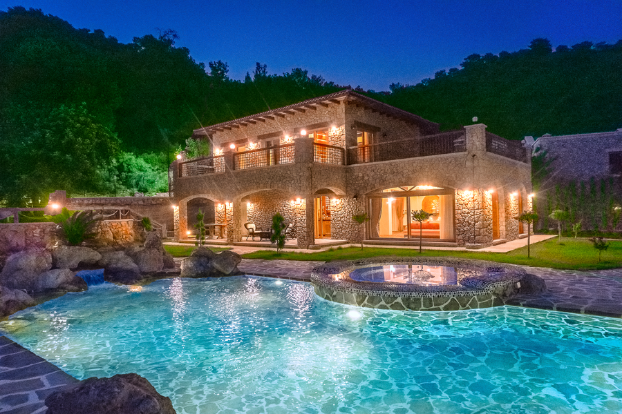 Stone villa illuminated at night beside a turquoise pool and spa terrace