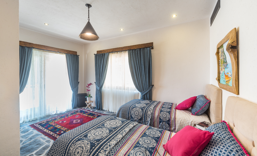 Bright twin bedroom with patterned textiles and large curtained windows