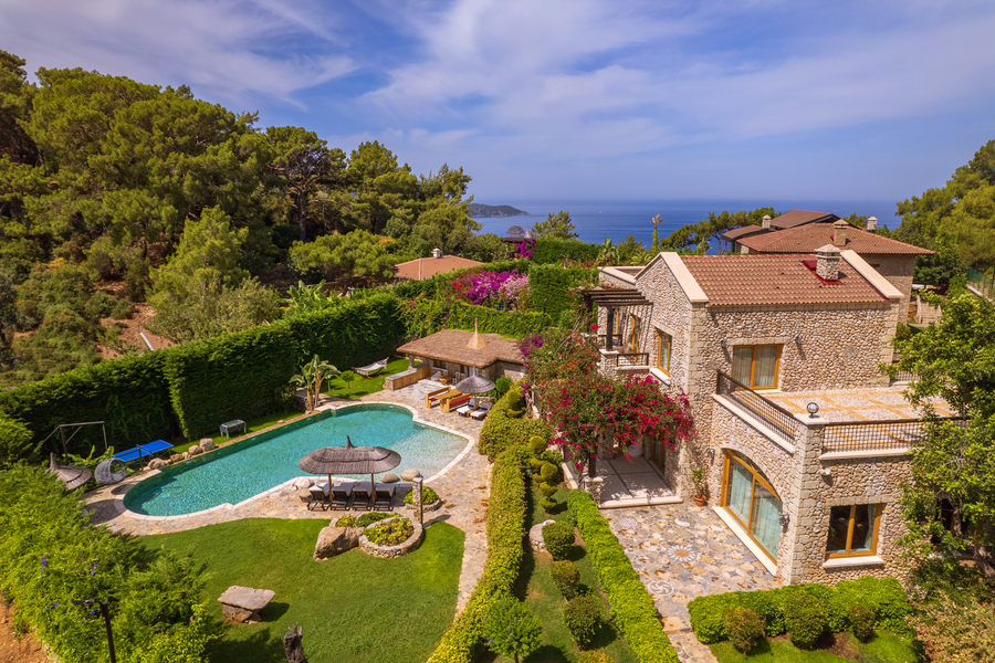 Aerial view of stone estate, organic-shaped pool and Mediterranean bay backdrop