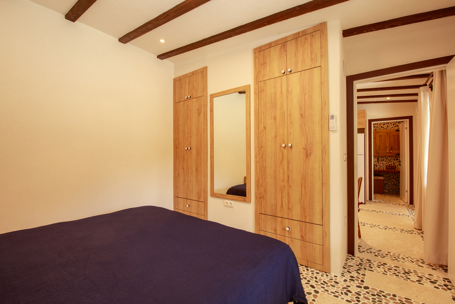 Minimal bedroom with wooden wardrobes and corridor view into mosaic bathroom