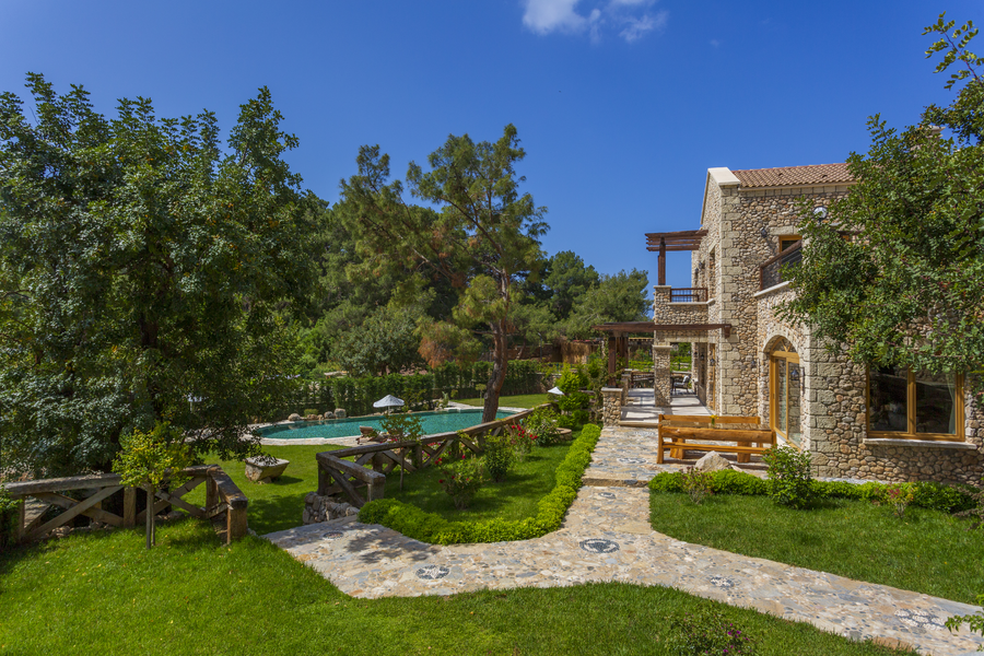 Stone villa with garden pathways overlooking a secluded pool on a forested peninsula