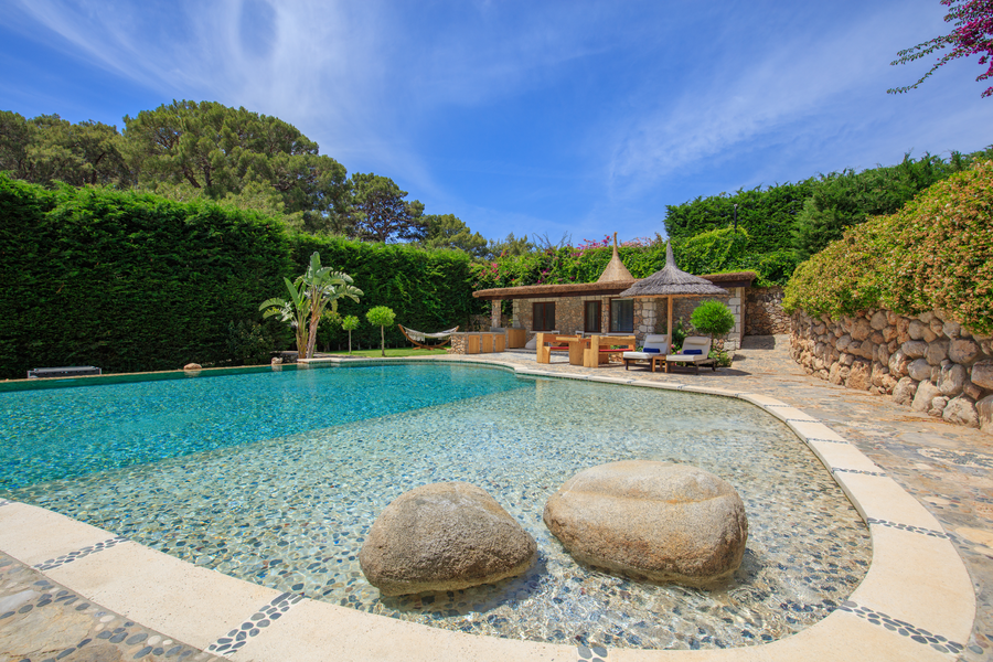 Organic-shaped pool with stone guesthouse and Mediterranean garden backdrop