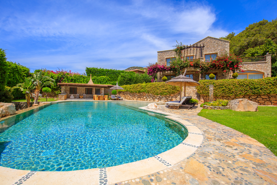 Organic-shaped pool with stone estate architecture and vibrant Mediterranean greenery