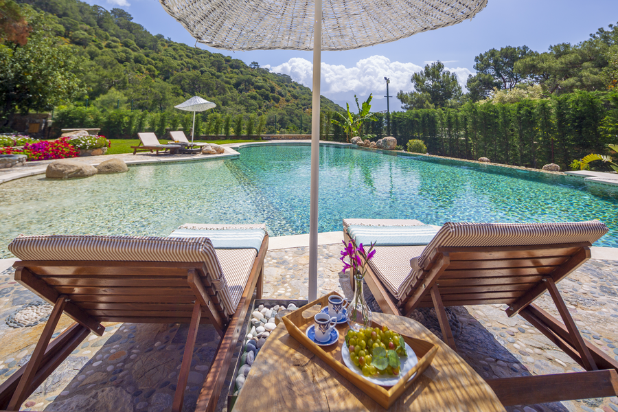 Poolside loungers overlooking a calm forest-side pool with a shaded coffee tray setting