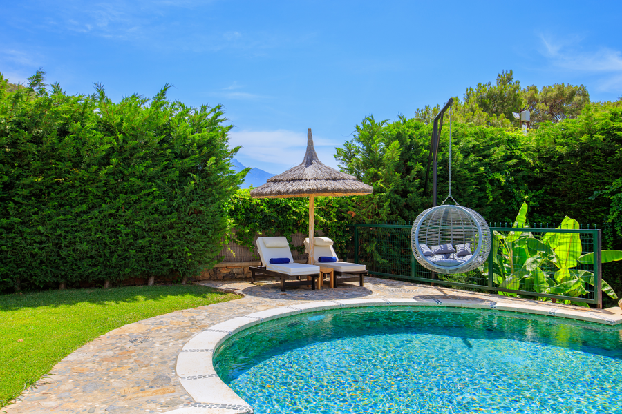 Poolside loungers and hanging chair surrounded by lush Mediterranean greenery