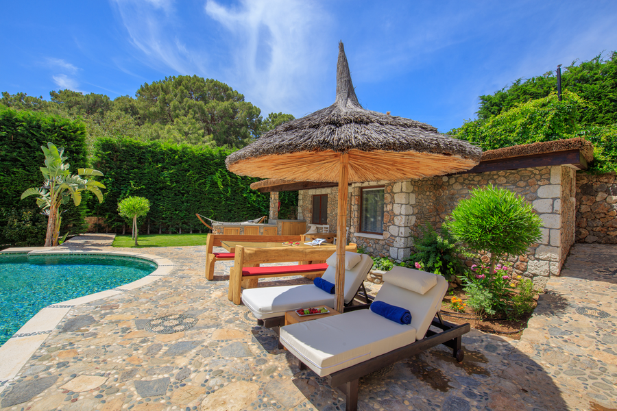Shaded poolside loungers beside stone guesthouse terrace at Villa Gemile