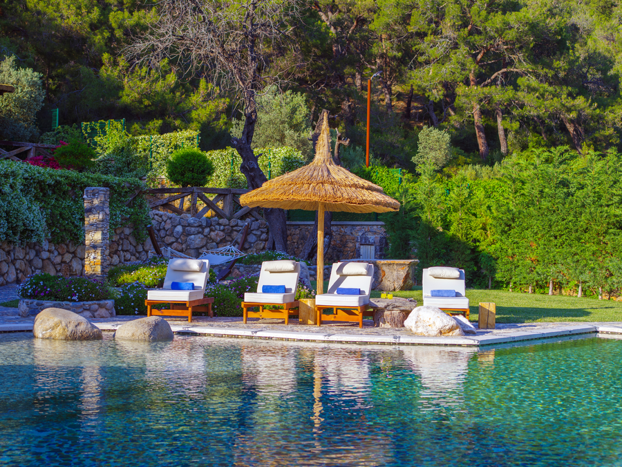 Poolside sunbeds beneath a rustic parasol beside a forested stone garden