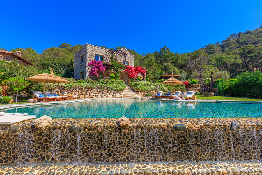 Stone villa above natural-style pool with cascading waterfall and vibrant bougainvillea