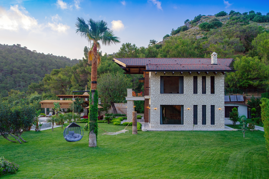 Stone villa facade framed by expansive gardens and a hammock under a tall palm tree
