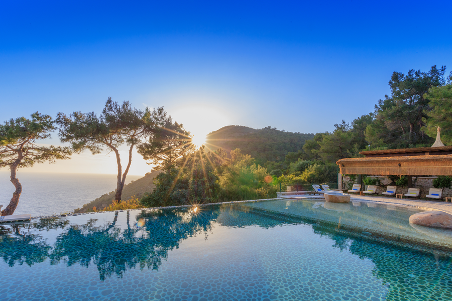 Infinity pool at sunrise overlooking Mediterranean sea and pine-covered cliffs