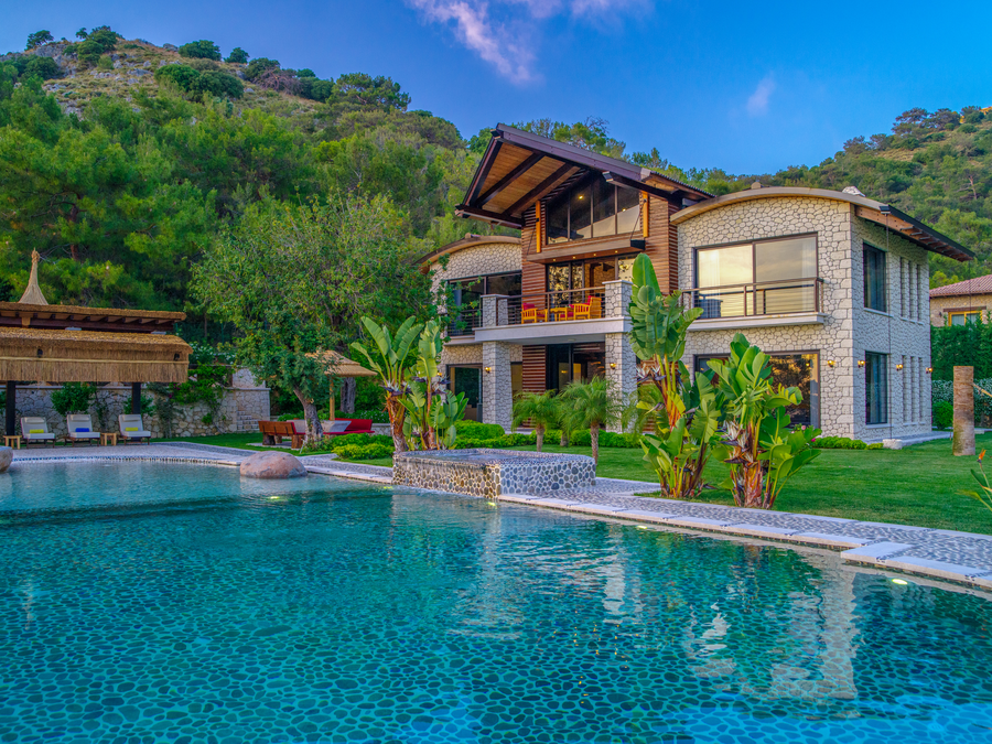 Stone villa facade rising above an infinity pool and lush tropical gardens