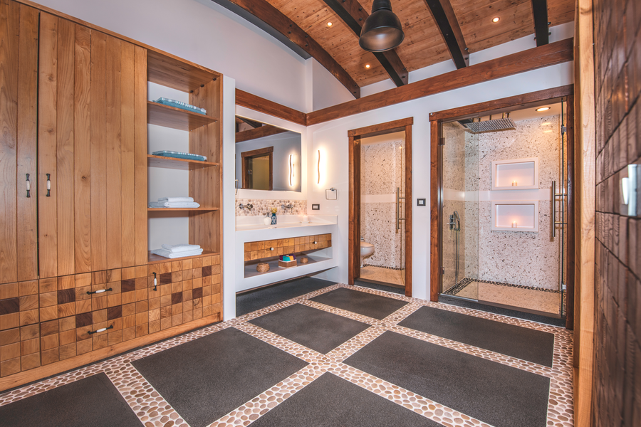 Spacious master bathroom with timber beams and minimalist stone-lined shower suites