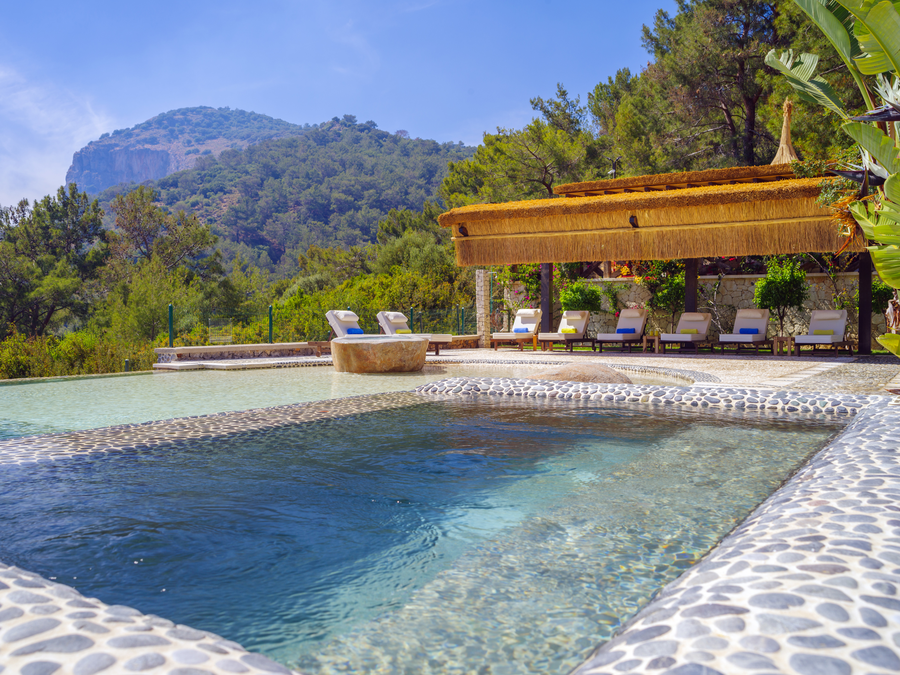 Multi-level stone pool overlooking forested mountains and shaded lounge terraces