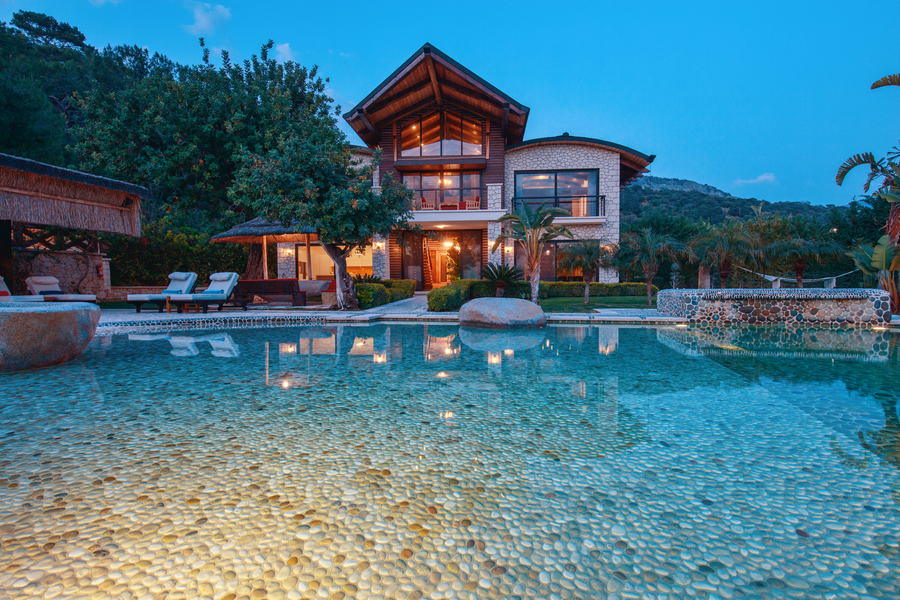 Natural-stone pool reflecting the main villa in a quiet Mediterranean setting