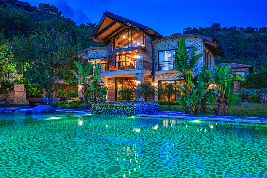 Illuminated stone villa façade rising above a tropical garden and glowing pool