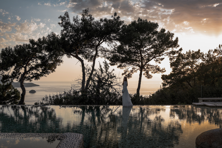 Sunset pool scene overlooking a secluded Mediterranean bay and pine forest
