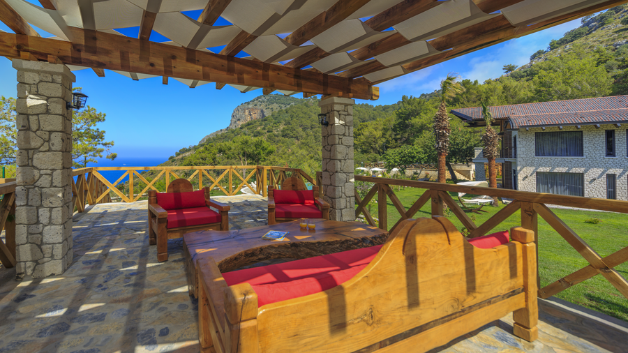 Shaded wooden terrace lounge overlooking sea and forested mountains